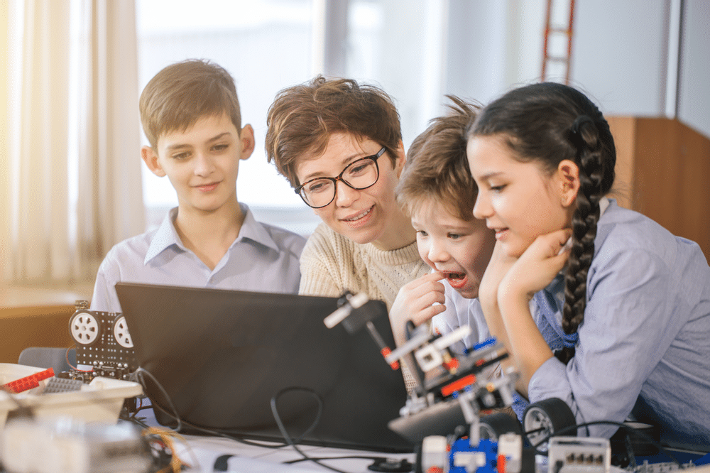 Three young child and one adult viewing something on a laptop in unison