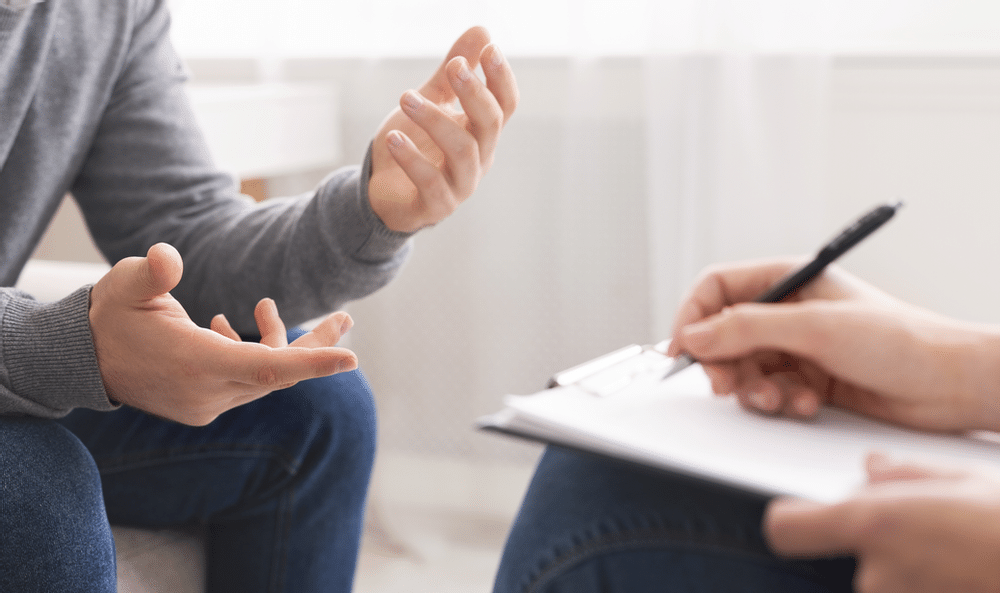 Two hands held out as if explaining something to another two hands taking notes on a notebook on lap.