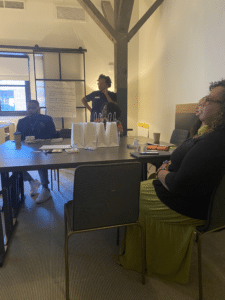 Two adults sitting at a table and one standing looking at something