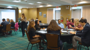 Room full of adults sitting at round tables talking