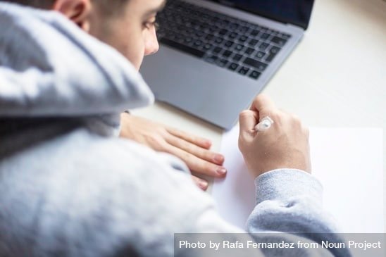 Student sitting at a desk with a laptop and a pen and paper.