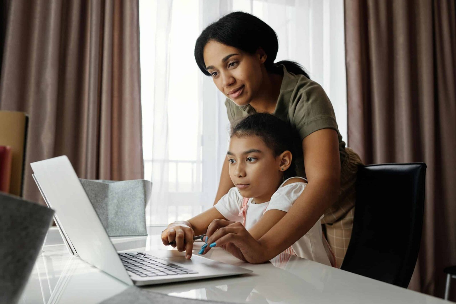 One child helping another child while looking at a laptop.