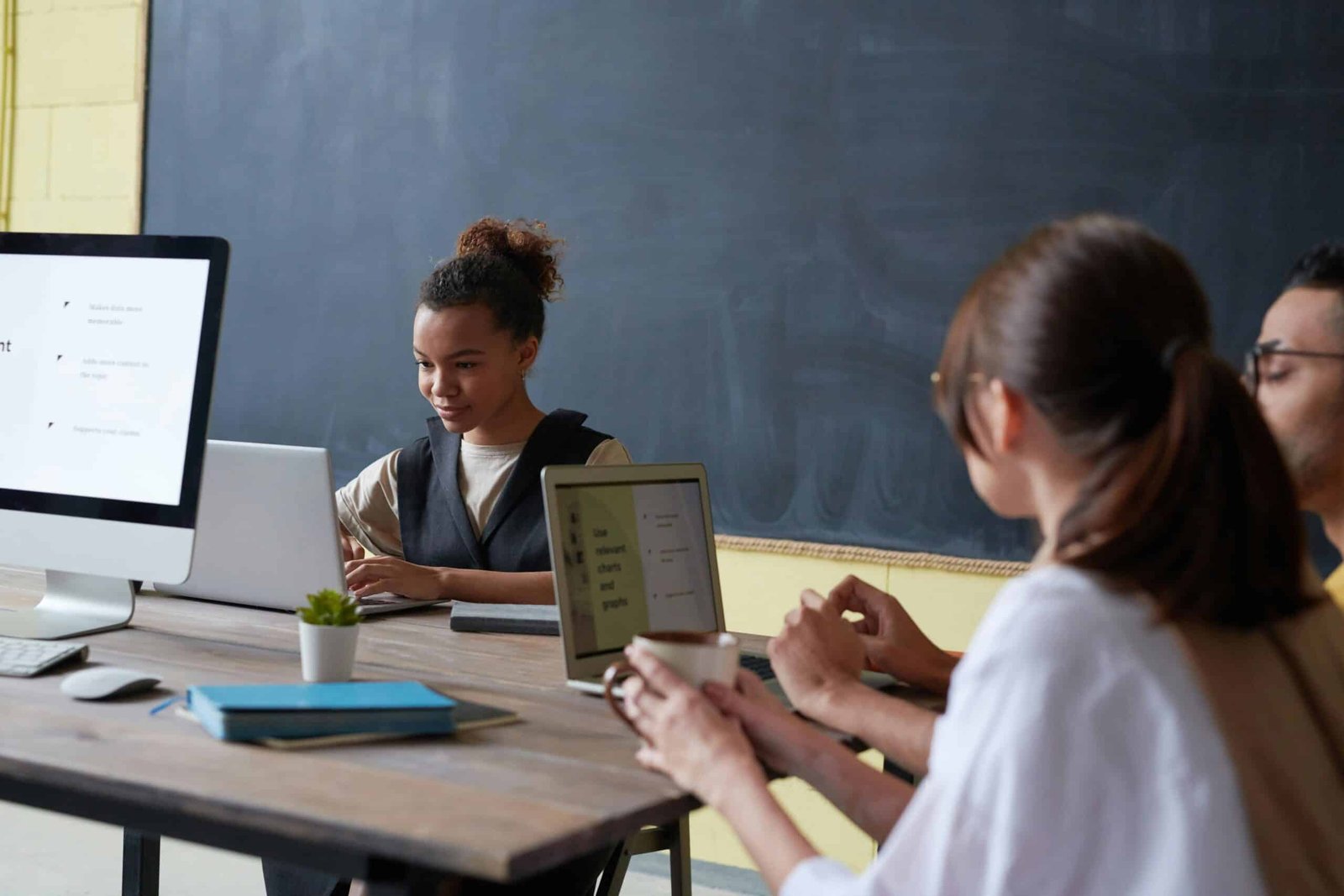 Students using laptops at their desks with the chalkboard in the background