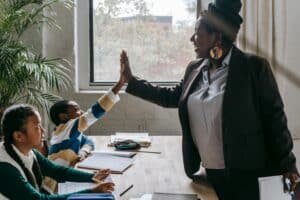 A woman in a business suit gives a high five to her students, celebrating their achievements in a classroom setting.