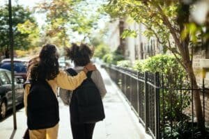 Two kids walking together, arm in arm, on the sidewalk